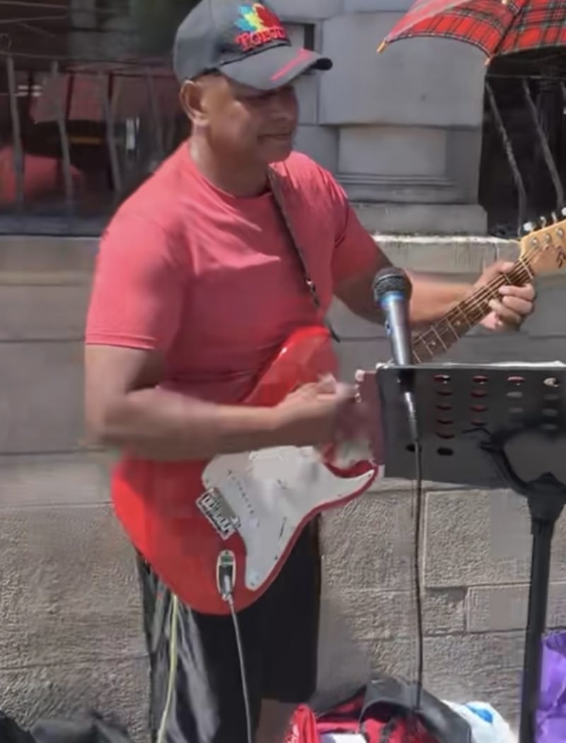 Street performer playing red electric guitar in urban ministry